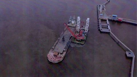 Foto udara crane barge memuat material keruk ke hopper barge di samping jetty terminal minyak, Dumai, Riau, 2025