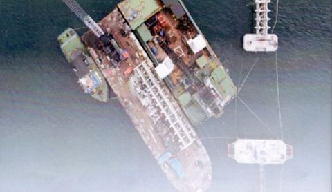 Foto udara tegak lurus crane barge dan deck barge bermuatan struktur baja di samping tiang jetty